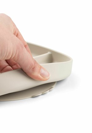 Harmaa, kolmionmuotoinen silikonilautanen pyöristetyillä reunoilla, jossa on kuvioitu alapuoli paremman pidon takaamiseksi. Käsi on asetettu reunan päälle tukemiseksi.