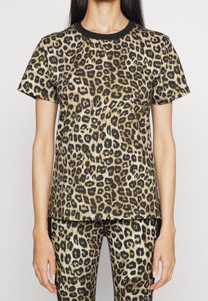 Kobieta nosząca dopasowany t-shirt z krótkim rękawem i legginsy w panterkę z czarnym kołnierzem, stojąca na jednolitym tle.