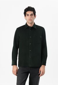 Green corduroy shirt with long sleeves, button-up front, pointed collar, and a chest pocket. Textured fabric and a relaxed fit.