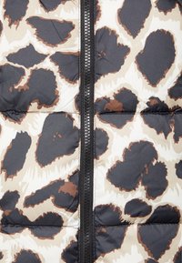 Lähikuva topatusta takista, jossa on musta vetoketju ja abstrakti suuri tummanruskea ja beige leopardikuvio.