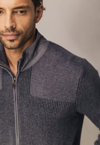 Grijze ritssweater met een textuur ribbelontwerp op het lichaam, gladde accenten op de schouders en een hoge kraag.