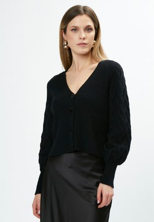 Zwarte cardigan met een V-hals, textuur in kabelbreisel op de mouwen en vier knopen aan de voorkant. De stof lijkt zacht en warm.