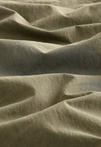Faltiger olivgrüner Stoff, der unter sanfter Beleuchtung detaillierte Textur und Falten zeigt.