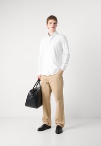 Weiße Langarm-Knopfhemd, beige Hose, schwarze Lederhandtasche und schwarze Schuhe. Minimalistisches Design, glatte Texturen, neutrale Farben.