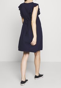 Granatowa sukienka z falbanami na krótkich rękawach, wcięciem w talii i luźnym krojem. W zestawieniu z czarno-białymi trampkami.