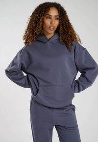 Mörkgrå hoodie gjord av mjukt material, med en stor framficka, dragsko i huvan och avslappnad passform med sänkta axlar.