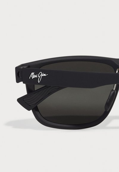 Occhiali da sole neri Maui Jim con montatura opaca, lenti scure, dettagli testurizzati sulle tempie e un logo distintivo.