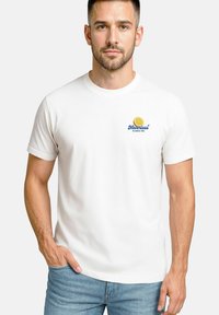 Weißes Baumwoll-T-Shirt mit kurzen Ärmeln, mit einem gelben Zitronen-Motiv und blauer Schrift "Newtless la dolce vita" auf der linken Brust.