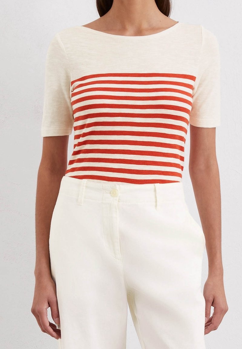 Top de manga corta a rayas en crema y rojo con un escote ancho. Combinado con pantalones blancos de tiro alto, con cierre de botón y bolsillos.