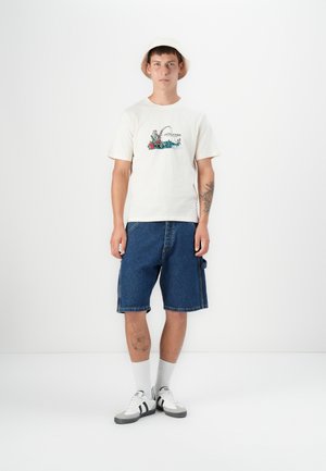 Weißes Baumwoll-T-Shirt mit einem bunten Angel-Graphic, kombiniert mit blauen Denim-Shorts, weißen Sneakern und einem beigen Bucket Hat.