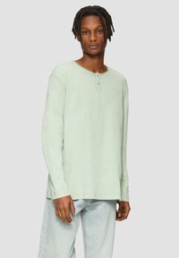 Bluzka z długim rękawem w miętowym kolorze z okrągłym dekoltem i listwą z trzema guzikami. Posiada luźny krój i miękką fakturowaną tkaninę.