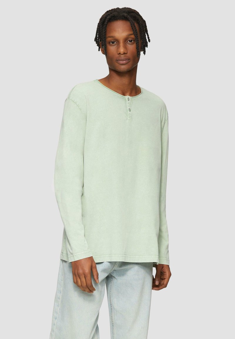 Bluzka z długim rękawem w miętowym kolorze z okrągłym dekoltem i listwą z trzema guzikami. Posiada luźny krój i miękką fakturowaną tkaninę.