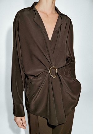 Bruine satin shirt met lange mouwen, een diepe V-hals, gedraaid ontwerp aan de voorkant en een decoratieve gouden gesp in de taille.