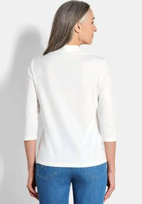 Weißes Oberteil mit drei Viertel Ärmeln, glatte Textur, runder Ausschnitt, kombiniert mit blauen Jeans aus Denim mit Rückentaschen. Minimalistischer Stil.