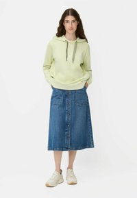 Jasnozielona bluza z kapturem i sznurkiem, zestawiona z niebieską spódnicą midi z dżinsu, z guzikami z przodu i kieszeniami po bokach. Noszona z białymi sneakersami.