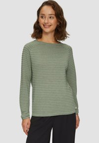 Haut à manches longues vert en maille côtelée avec un col rond. Le tissu texturé présente des rayures horizontales. Assorti à un pantalon noir.