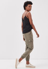 Un débardeur noir à fines bretelles, associé à un pantalon cargo vert olive avec des poches latérales, et des baskets légères de couleur claire.