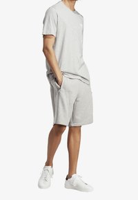 Šedé bavlněné tričko s kulatým výstřihem, spárované s odpovídajícími šedými šortkami s bočními kapsami a bílými trojpruhymi. Bílé tenisky.