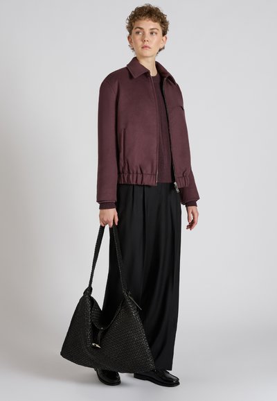 Burgundowa kurtka bombowiec z elastycznym pasem, zapięciem na zamek błyskawiczny i bocznymi kieszeniami; w połączeniu z luźnymi czarnymi spodniami i teksturowaną czarną torebką.