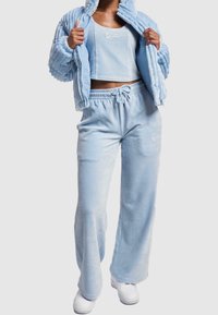 Svetlemodrý kordurovský teplákový komplet skládající se z crop topu, zipové bundy a kalhot s širokými nohavicemi, elastickým pasem a šňůrkou. Součástí jsou také tenisky.