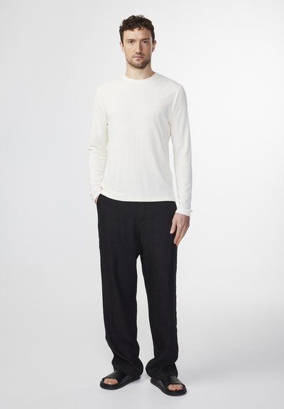 Long-sleeved cream shirt, relaxed fit, paired with loose black pants and black sandals. Smooth texture, minimal design, neutral colors.