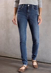 Jeans ajustados de denim azul oscuro, con una cintura alta, diseño clásico de cinco bolsillos y detalles de costura, combinados con unas bailarinas de estampado de leopardo.