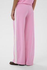 Ružové široké nohavice vyrobené z mäkkej látky s bielym vertikálnym pruhom po stranách. Hlavnou črtou je uvoľnený strih a olemované spodné okraje.