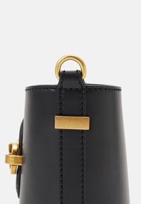 Černá kožená kabelka se zlatými detaily. Obsahuje kulatý kroužek a obdélníkový akcent, prošívané detaily podél okrajů.