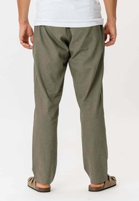 Herre let olivengrøn bukser, lavet af et blødt stof, med et afslappet design og lige ben. Bæres med enkle brune sandaler.