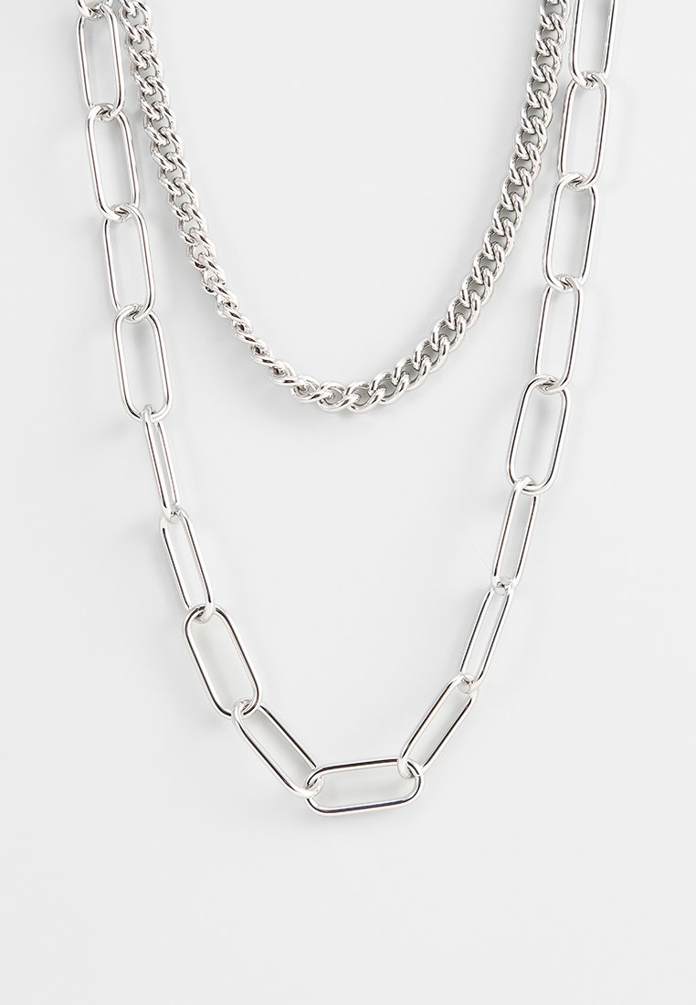 Silberne Kettenhalskette mit zwei geschichteten Designs: einer glatten ovalen Gliederkette und einer strukturierten Gliederkette, beide mit polierten Oberflächen.