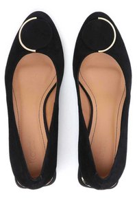 Ballerine nere in suede con punta rotonda, lati intagliati e dettaglio in anello dorato sulla parte anteriore. Interno in pelle liscia e dettagli di cucitura minimi.