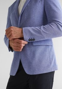 Light blue blazer with a textured weave, single-breasted design, notched lapels, and four black buttons on the cuff.