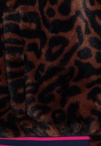Brahk umetni krzneni material z vzorcem črnih leopardskih pik; ima gladko teksturo in mornarsko modro obrobo z rožnatimi črtami.