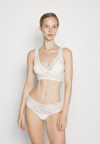 Bijela čipkana bralette i odgovarajući set gaćica s mekanim, teksturiranim čipkastim dizajnom, prozirnim detaljima i valovitom ivicom na pojasu.