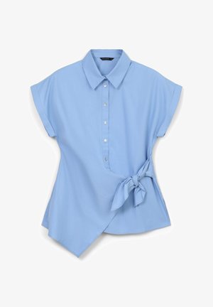 Blusa azzurro chiaro con colletto, maniche corte arrotolate, chiusura frontale con bottoni e orlo asimmetrico. Presenta un nastro decorativo in vita.