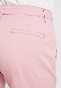 Vaaleanpunaiset puuvillapantsit, joissa on normaali vyötärö ja yksi takatasku suorakaiteen muotoisella läpällä, sileä rakenne ja minimalistinen muotoilu.