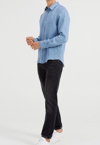 Ljusblå långärmad skjorta i linne knäppt fram, kombinerad med svarta jeans och vita sneakers. Skjortan har en avslappnad passform och subtil textur.