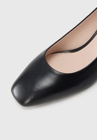 Black leather pump with a square toe, smooth texture, and a subtle sheen. Features a low-cut front and a beige interior lining.