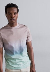 Vieglas Crew-neck t-krekls ar ombre gradientu, kas pāriet no gaiši bežīgas līdz bālzaļai. Kokvilnas sakausējums, gluda tekstūra.