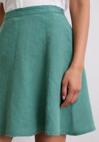 Een groene linnen rok met een uitlopende design, voorzien van een gestikt tailleband en een gladde textuur, accentueert door zijnaad en een knielange zoom.
