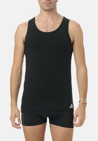 Black tank top made of cotton, featuring a round neckline and Adidas logo on the lower left. Sleeveless design with a fitted cut.