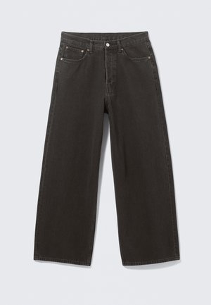 Svarte vide denimjeans. Har standard midje, fem lommer og metallbeslag. Sømdetaljer langs sømmene.