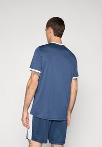 Sötétkék sportpóló rövid ujjal, fehér szegéllyel, és hozzáillő rövidnadrággal. Simás textúrával és laza szabással rendelkezik, amely sportolásra alkalmas.