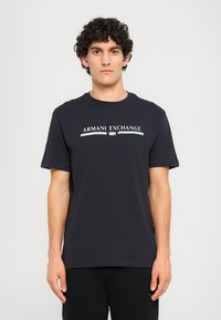 Mørkeblå t-skjorte i bomull med korte ermer, rund hals og hvit "Armani Exchange 1991" logo trykket på brystet.
