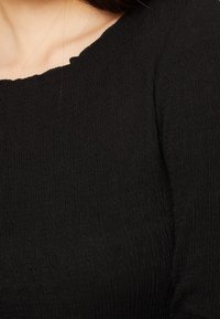 Top nero con un motivo testurizzato, caratterizzato da un colletto a scollatura ondulata e una forma aderente, che mette in mostra un tessuto morbido e a coste.