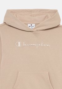 Beige hoodie met een voorkruiszak en een capuchon met trekkoord. Voorzien van het geborduurde "Champion" logo in lichte draad. Zachte, katoenmix materiaal.