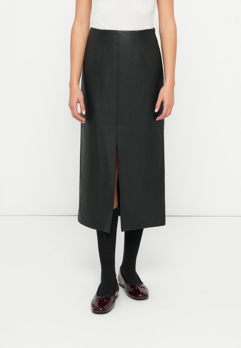 Svart skinn midi skjørt med en frontslit, jevn tekstur og en tettsittende design, kombinert med svarte sokker og burgunder leiligheter.