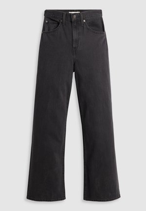 Mustat farkut leveillä lahkeilla ja korkealla vyötäröllä, viisi taskua ja metallinen nappikiinnitys. Kangas on sileä, hieman haalistunut.