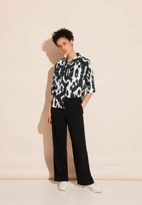 Black and white patterned shirt with short sleeves and a collar, paired with wide black trousers and white sneakers on a neutral background.