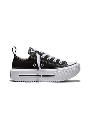 Zapatilla negra baja de lona con suela de goma blanca, cordones blancos y una franja negra, mostrada de perfil sobre un fondo blanco.